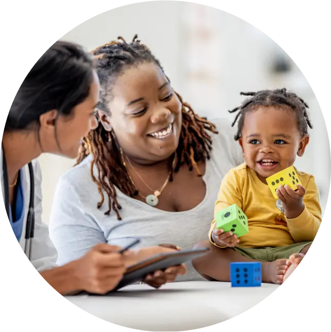 mother and her smiling baby sit together with a doctor