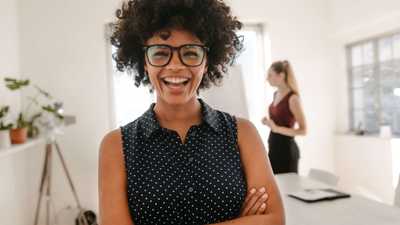 Young woman with glasses laughs with arms crossed